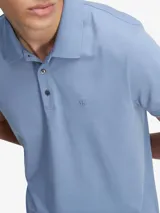 Chomba de corte slim color azul, confeccionada en tejido de punto fino con cuello clásico, cierre frontal de botones y mangas cortas. Presenta un logotipo monograma bordado en el pecho y dobladillo con aberturas laterales.