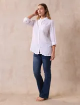 Camisa blanca de lino con cuello con solapa, manga larga regulable con presilla y botón, y abertura central con botones.