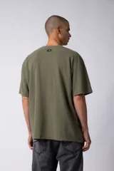 Remera de corte oversize color marrón, con cuello redondo y mangas cortas con hombros caídos. Presenta un bordado minimalista de un joystick en el centro del pecho y una etiqueta aplicada en la parte superior de la espalda.