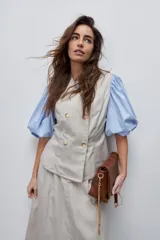 Chaleco de calce entallado color beige, de estilo cruzado con doble botonadura y escote redondo.