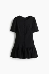 Vestido corto negro con escote redondo, mangas cortas abullonadas y cierre frontal de botones forrados. Cuenta con costuras moldeadoras en la cintura y falda con bajo globo fruncido.