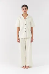 Conjunto de dos piezas color blanco off-white, compuesto por una camisa de manga corta con cuello camisero y bolsillos frontales, y un pantalón largo de corte recto y holgado.