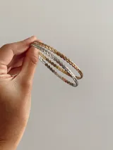 Esclava rígida con diseño trenzado, fabricada en acero quirúrgico. El set incluye dos unidades, una en tono dorado y otra en tono plateado.
