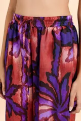 Pantalón de corte amplio y tiro alto con cintura elástica y cordón ajustable. Presenta un estampado botánico de hojas en tonos púrpuras y rojizos sobre una base cobriza, con una caída fluida y relajada.