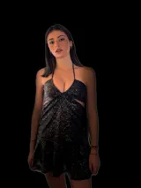 Vestido corto negro con diseño cut-out en la cintura y detalle de encaje en el centro del busto. Presenta breteles finos, falda con volado en el ruedo y flecos decorativos.