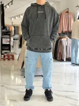 Canguro oversize gris con efecto acid wash, capucha y gran estampado blanco en la espalda con tipografía y estrella estilizada.