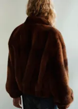 Chaqueta de efecto pelo en color marrón, de corte recto, con cuello alto, mangas largas con puños elásticos y cierre delantero con botones. Cuenta con dos bolsillos de solapa en la parte frontal.