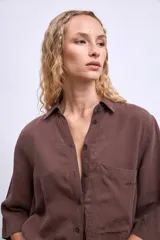 Camisa marrón de manga 3/4, con cuello clásico, botones frontales y un bolsillo en el pecho.