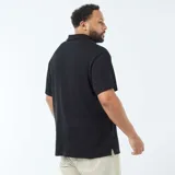 Polo negro de manga corta con cuello y tapeta de tres botones. El tejido presenta una textura de punto waffle o piqué sutil.