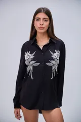 Camisa negra de manga larga con cuello clásico y botones frontales. Presenta dos grandes apliques bordados con lentejuelas y cuentas en forma de flores y hojas en la parte delantera.