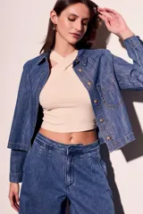 Camisa de jean azul de corte recto, con cuello clásico, cierre frontal con botones marrones, bolsillo de parche en el pecho y mangas largas con puños abotonados.