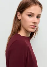 Vestido corto entallado de color bordó, con cuello barco y mangas largas. Presenta detalles de fruncidos laterales en la cintura.