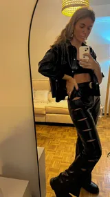 Pantalón de cuero sintético negro, de tiro alto y corte acampanado, con aberturas geométricas en las piernas.