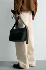 Bandolera de piel color marrón oscuro con acabado abatanado. Cuenta con una solapa con cierre de imán y cremallera, y un bolsillo interior con cremallera. El asa de hombro es ajustable.