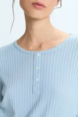 Pijama compuesto por una remera de manga larga en color celeste con textura acanalada y cierre frontal con botones, y un pantalón largo de corte recto en color blanco con rayas verticales celestes y cintura elástica con cordón ajustable.