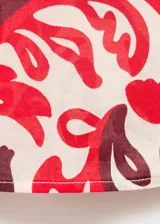 Camisa de corte recto y diseño holgado, confeccionada en algodón con estampado floral en tonos rojos y bordó sobre fondo crudo. Presenta cuello camisero clásico, cierre frontal con botones y mangas largas.