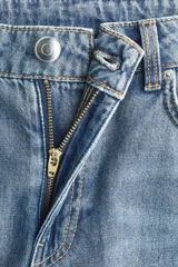 Jeans de denim rígido, color azul claro con efecto desgastado (lavado claro). De tiro medio/alto, corte recto y pierna ancha desde la cadera hasta el bajo. Presenta cinco bolsillos y cierre frontal con botón.