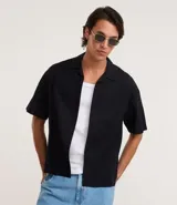 Camisa de manga corta color negro, con diseño boxy, cuello clásico y abotonado frontal.