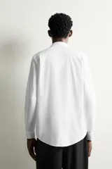 Camisa de vestir blanca de corte slim fit, confeccionada en tejido de algodón con textura estructurada. Cuenta con cuello italiano, mangas largas con puños abotonados y cierre frontal con botonadura.