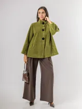 Chaqueta tipo capa confeccionada en paño, con cuello alto, cierre frontal de botones grandes y mangas amplias. Cuenta con bolsillos laterales y forro interior.