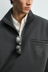 Sudadera de corte relajado color negro, con cuello alto y cierre frontal de cremallera. Presenta un bolsillo de vivo en el pecho con un estampado a contraste y acabados elásticos en puños y ruedo.