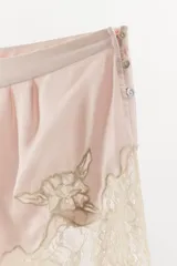 Shorts de tiro medio confeccionado en satén, con detalle de encaje y bordados florales a contraste en el ruedo. Presenta cierre lateral con botones.