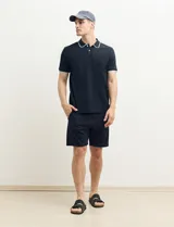 Remera polo azul marino con ribetes blancos en el cuello y en los bordes de las mangas corta, y cierre frontal de botones.