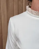Polera de manga larga color blanco, confeccionada en algodón, con cuello alto tipo tortuga y detalles de volados en el cuello y en los puños.