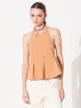 Top color tostado, con cuello halter, espalda descubierta y faldón con tablas superpuestas.