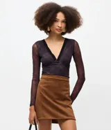 Body de tul negro con transparencia, manga larga y escote en V profundo con detalle de encaje en el borde. Presenta un diseño ajustado al cuerpo con cierre de broches a presión en la parte inferior.
