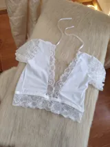Top blanco de encaje con escote profundo en V, mangas cortas de encaje y detalle de puntilla en el ruedo. Cuenta con tiras finas para atar al cuello.