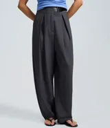 Pantalón sastre de corte barrel, color gris oscuro, con cintura alta, pinzas delanteras y diseño de pierna ancha.