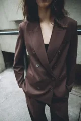 Blazer de corte sastre con cuello solapa, manga larga y hombreras marcadas. Presenta un diseño cruzado con cierre frontal de botones, bolsillos delanteros de vivo y abertura posterior en el bajo.