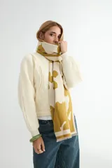 Bufanda rectangular de tejido de punto, con diseño estampado de manchas abstractas en color mostaza sobre fondo crudo y terminación con flecos cortos.