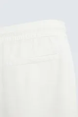 Bermuda de algodón color beige claro, de corte regular fit, con cintura elástica ajustable mediante cordón. Presenta bolsillos laterales y un bolsillo trasero de vivo.
