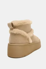 Botín plano de gamuza color beige, con interior y bordes forrados en pelo sintético. Presenta suela de plataforma engomada y tirador trasero.