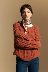 Cardigan de punto color terracota con diseño de trenzas verticales, cuello redondo y cierre frontal con botones metálicos. Presenta mangas largas con puños ajustados y un calce holgado.