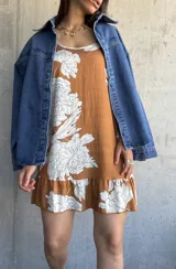 Vestido corto color camel con estampado de flores blancas, sin mangas, con cuello redondo y volados en el ruedo.