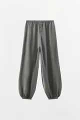 Pantalón de tiro alto confeccionado en tejido de punto mezcla de algodón, con cintura elástica y detalle de botones frontales. Presenta un diseño de pernera amplia con bajo abullonado acabado en elástico.