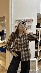 Camisa de corte relajado confeccionada en algodón con estampado de cuadros tartán en tonos marrones y beige. Presenta cuello clásico, cierre frontal de botones, mangas largas con puños abotonados y un bolsillo frontal en el pecho.