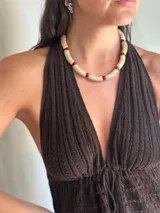 Collar corto tipo gargantilla compuesto por cuentas tubulares de color beige con textura craquelada, separadas por cuentas pequeñas de cristal rojo.