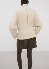 Chaqueta beige de cuello alto, manga larga con puños abotonados, bolsillo con solapa en el pecho, cinturón ajustable para la cintura y cierre frontal de cremallera oculta.