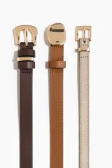 Pack de tres cinturones finos de diseño clásico, con hebillas metálicas doradas. Incluye uno en color marrón oscuro, uno en tono tostado texturizado y uno en color beige.