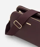 Cartera bandolera de tamaño mediano en cuero sintético color bordó, con formato rectangular y múltiples compartimentos con cierre de cremallera. Incluye correa de hombro ajustable en grosgrain y herrajes metálicos dorados.