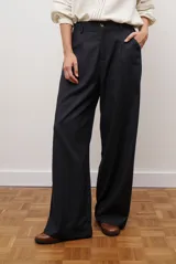 Pantalon de corte recto y pierna ancha, confeccionado en tejido tipo denim oscuro. Presenta tiro alto, cintura con cierre frontal y bolsillos laterales funcionales.