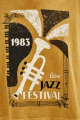 Remera de algodón color mostaza con estampa frontal estilo vintage que incluye un diseño de trompeta, piano y la inscripción '1983 Live Jazz Festival'. Presenta cuello redondo y mangas cortas.