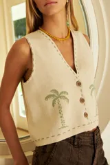 Chaleco de punto color crema con diseño de palmeras en verde claro. Presenta escote en V, abotonadura frontal con botones marrones y ribetes de punto en verde claro.
