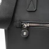 Cartera tipo tote de diseño estructurado en color negro, confeccionada en material sintético. Cuenta con doble asa superior fija, correa larga regulable y extraíble, bolsillo frontal con cierre metálico y logo circular grabado en la parte inferior.
