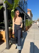 Pantalón de jean azul oscuro con bolsillos delanteros y traseros, cierre frontal con botones a la vista y corte acampanado con dobladillo en celeste.