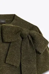 Jersey de punto de manga corta y cuello redondo, en color verde oliva. Presenta un detalle de lazo grande en el frente que le otorga un toque distintivo y femenino.
